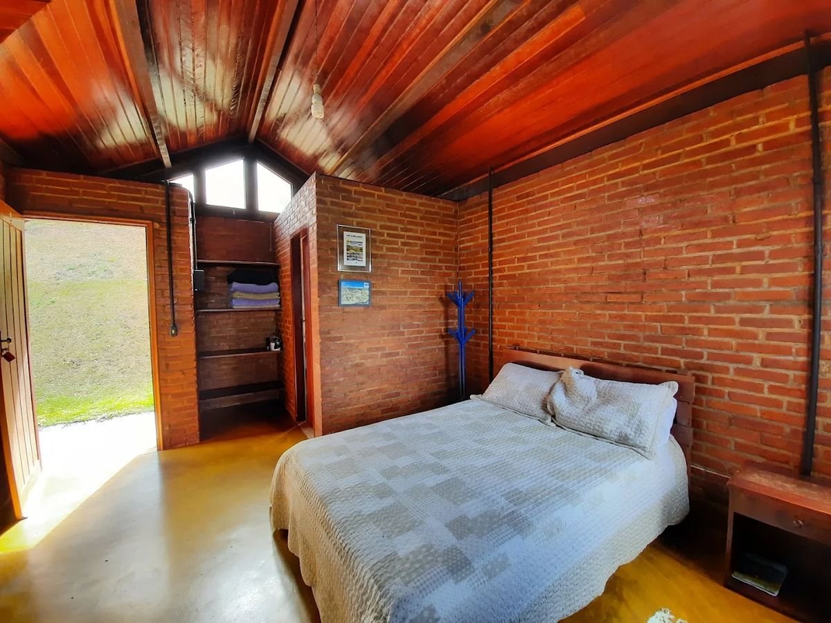 Quarto de tijolos aparentes com teto de madeira e porta aberta para o gramado